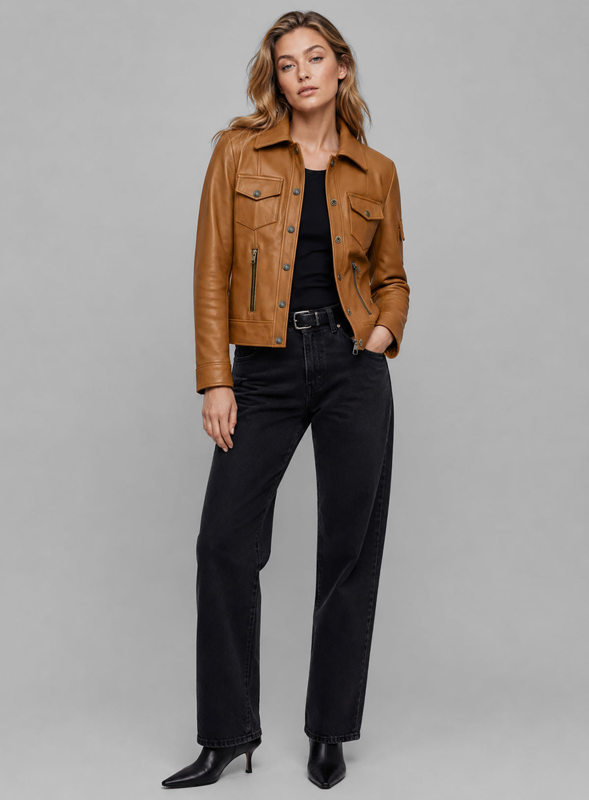Woman wearing a tan leather trucker jacket with snap buttons and chest flap pockets, full-length view