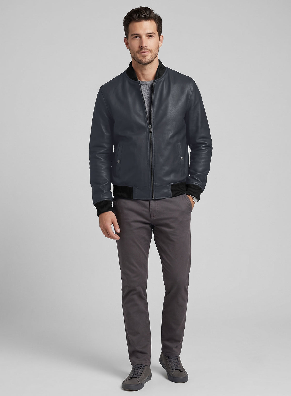Full-length view of a man wearing a grey-blue leather bomber jacket with grey trousers