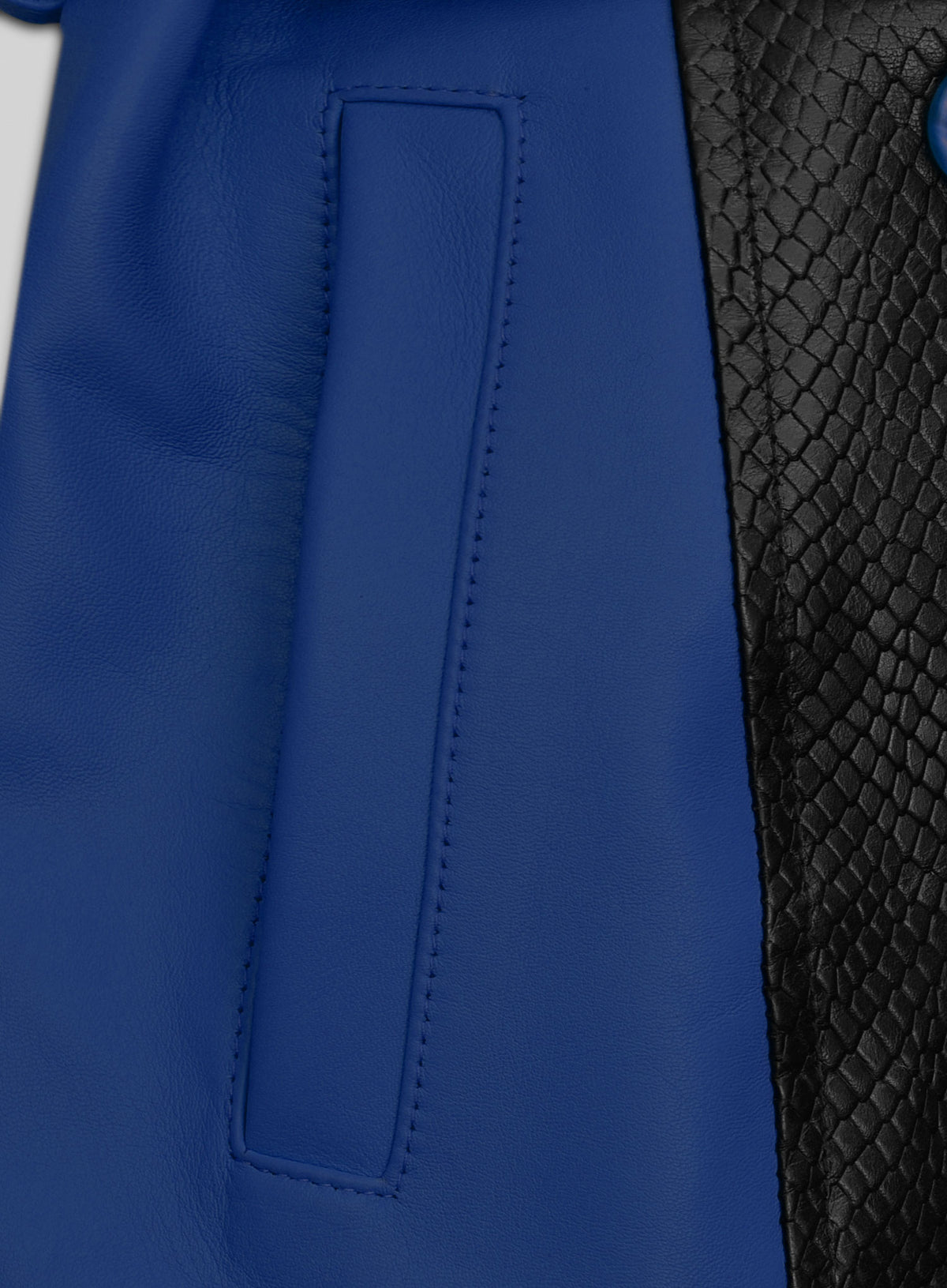 Close-up of blue leather trench coat pocket beside black snake-embossed leather panel