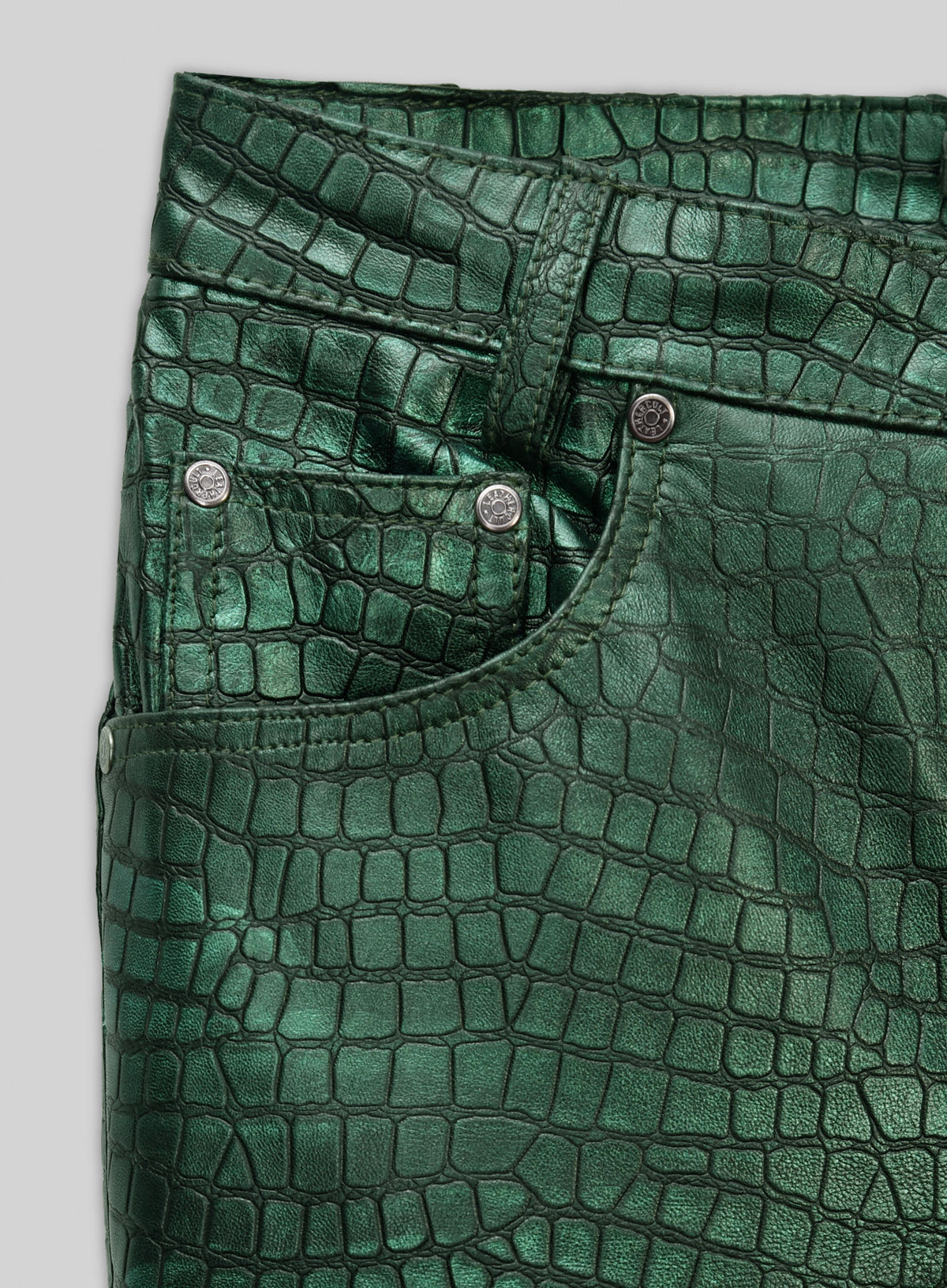 Close-up of metallic green croc-embossed leather pants pocket and rivets
