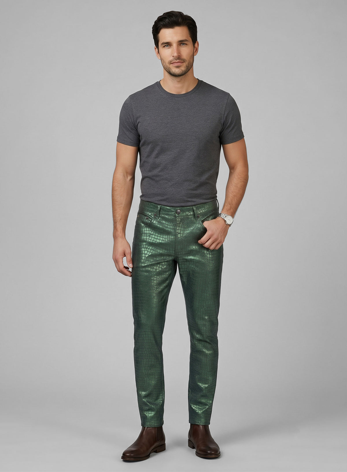 Full-length view of a man in metallic green croc-embossed leather pants, grey tee and brown boots