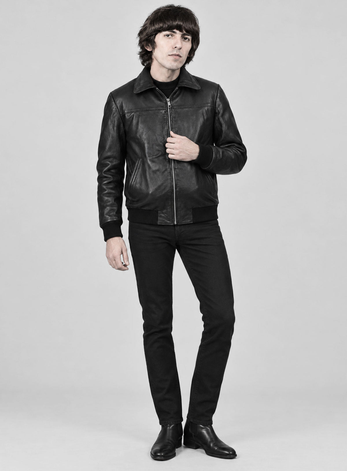 Full-length view of a man in a black leather bomber jacket with black jeans, George Harrison inspired