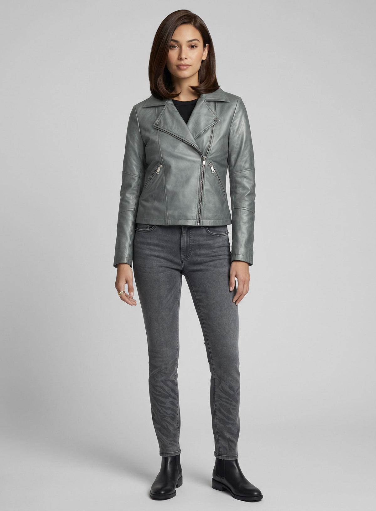 Full-length view of a woman in a metallic grey leather biker jacket, grey jeans and black ankle boots