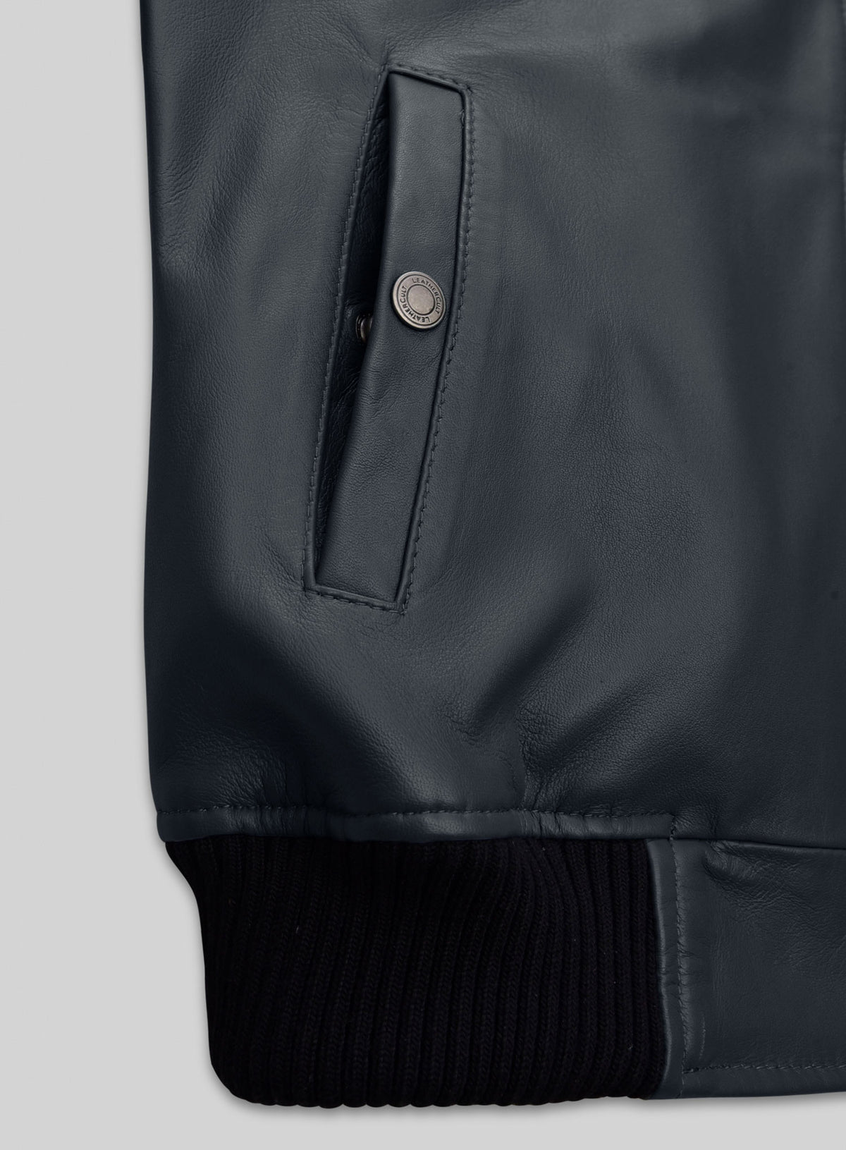 Close-up of a snap-button welt pocket and ribbed hem on a grey-blue leather bomber jacket