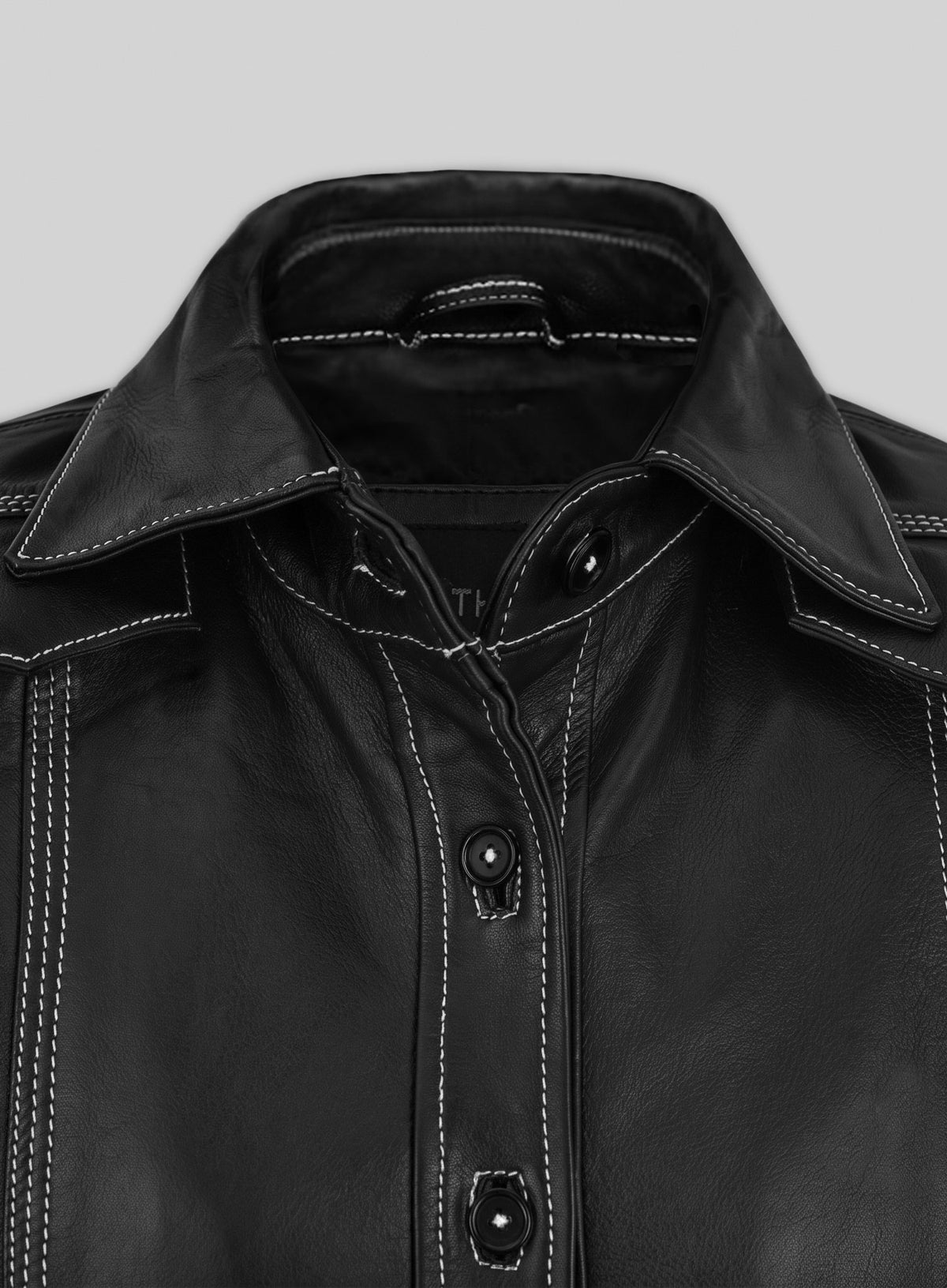 Close-up of the collar and button placket of a black leather shirt with white stitching