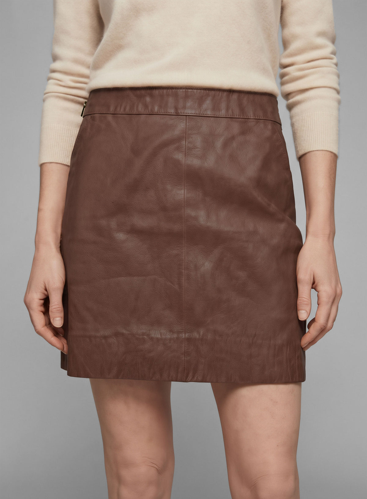 Close-up of a tan brown washed wax leather mini skirt on a model, with side zipper