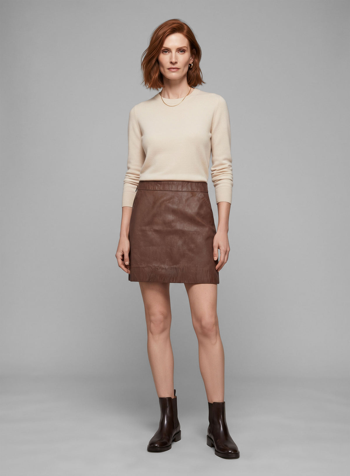 Woman wearing a tan brown washed leather mini skirt with a cream sweater and black boots