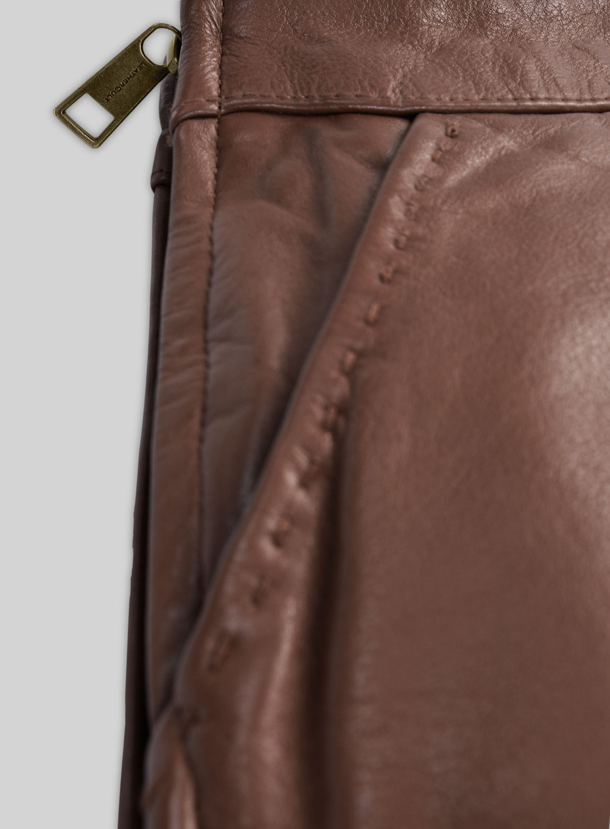Close-up of brass side zipper pull and stitched pocket on a tan brown leather skirt