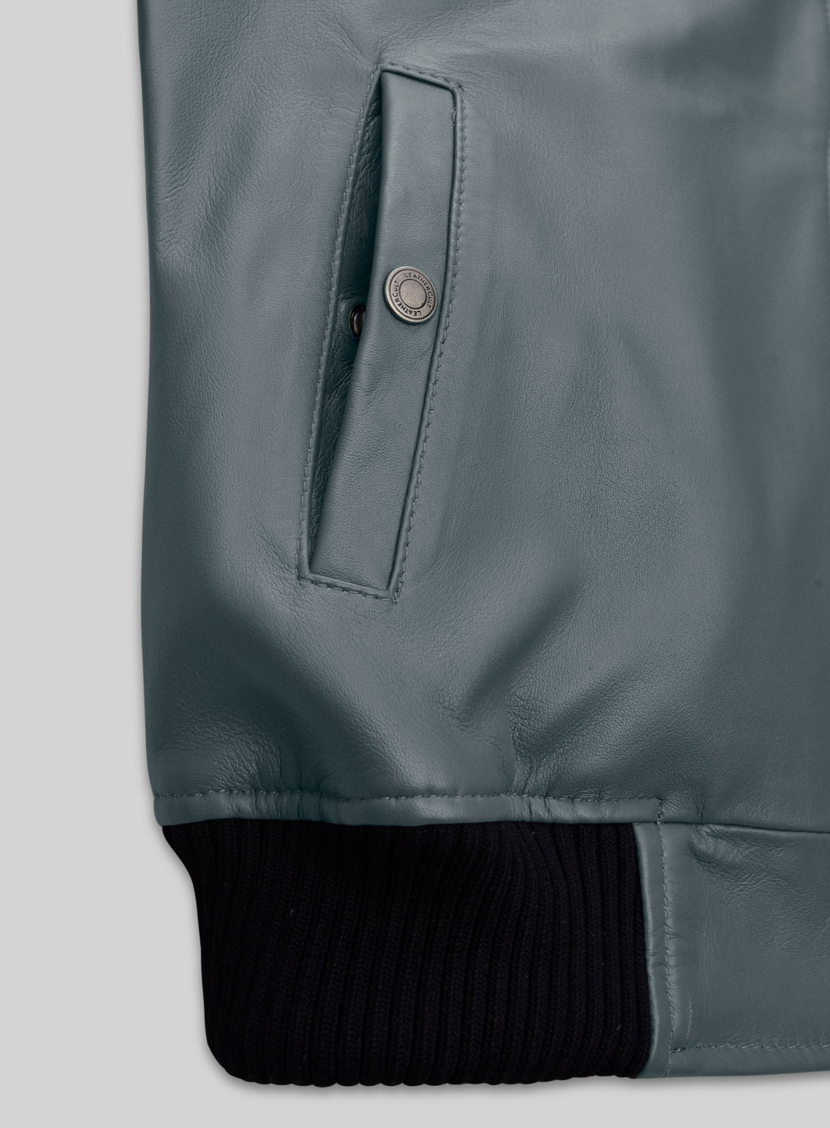 Close-up of grey leather bomber jacket slit pocket with snap button and ribbed hem