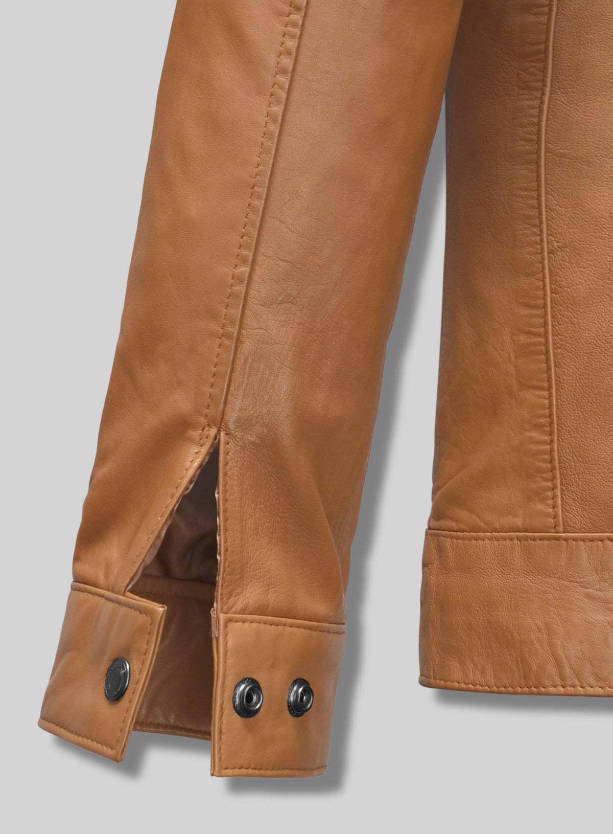 Close-up of tan leather jacket cuff with snap buttons and sleeve vent
